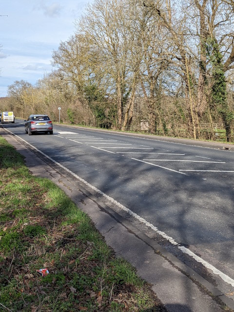 Photo of Epping New Road showing overgrown shared use footway and lanes narrowed by central hatch markings.
